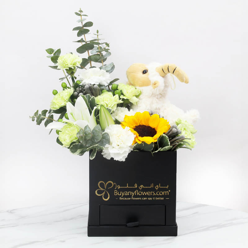 Dhiya’ Al-AdhaGifts and Hampers1 Sheep Plush Toy 20cm, Premium Assorted Chocolates By Sweecho 100gm, 1 Sunflower, 1 White Lily, 5 Green Carnations, 4 White Carnations , 2 Green Hypericum, Leaves -1 Eucalyptus and 2 Pittosporum, Prepared in a Black Square