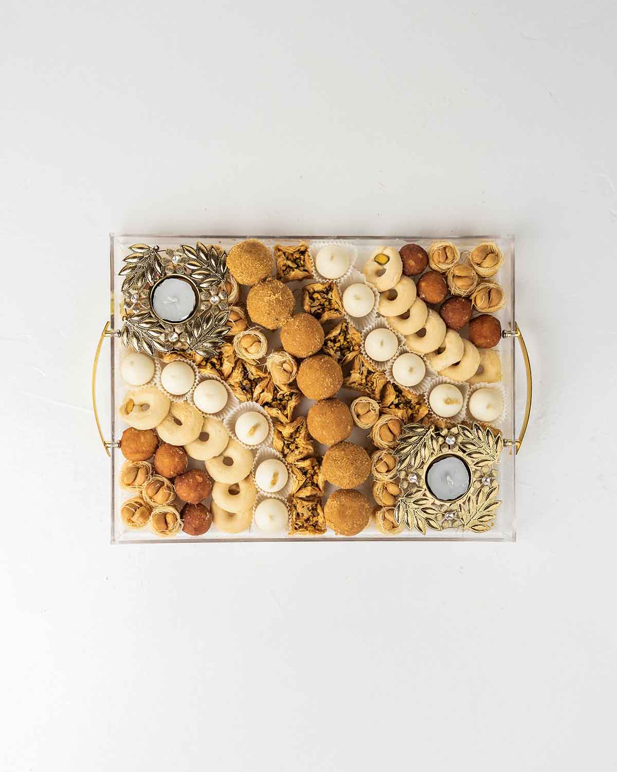 Diwali'24 Tray GiftChocolate & ConfectioneryYour Gift Contains:• 2 x designer metal Diya• 18 x Esch Cashew• 8 x Gulab Jamun• 7 x Besan Laddu • 13 x Ghraieb• 15 x Bookaj Pistachio• 12 x White chocolate assorted truffles filled in Pistachio, Kunafa, Hazelnu