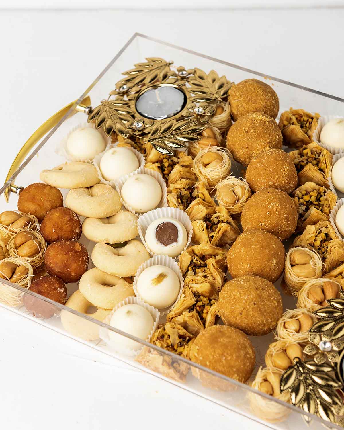 Diwali'24 Tray GiftChocolate & ConfectioneryYour Gift Contains:• 2 x designer metal Diya• 18 x Esch Cashew• 8 x Gulab Jamun• 7 x Besan Laddu • 13 x Ghraieb• 15 x Bookaj Pistachio• 12 x White chocolate assorted truffles filled in Pistachio, Kunafa, Hazelnu