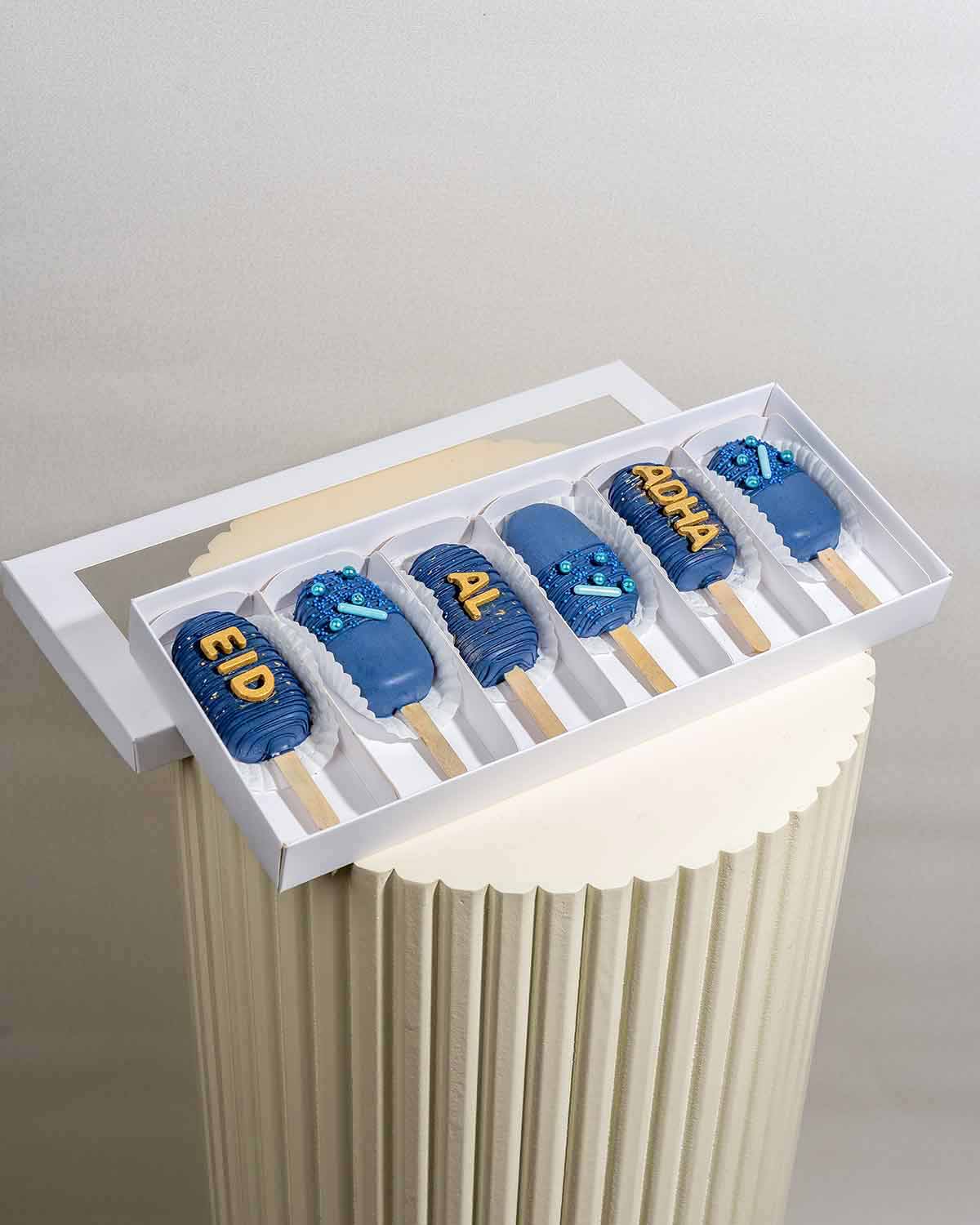 Designer Blue CakesiclesChocolate & ConfectioneryYour Gift Contains:• 6pcs Eid al adha Theme Cakesicles• Flavors available: Chocolate/Vanilla/Red Velvet• Chocolate Weight: 350g• Box Size: 35x14.5x4cmHandling and Storage • Keep away from direct heat and su