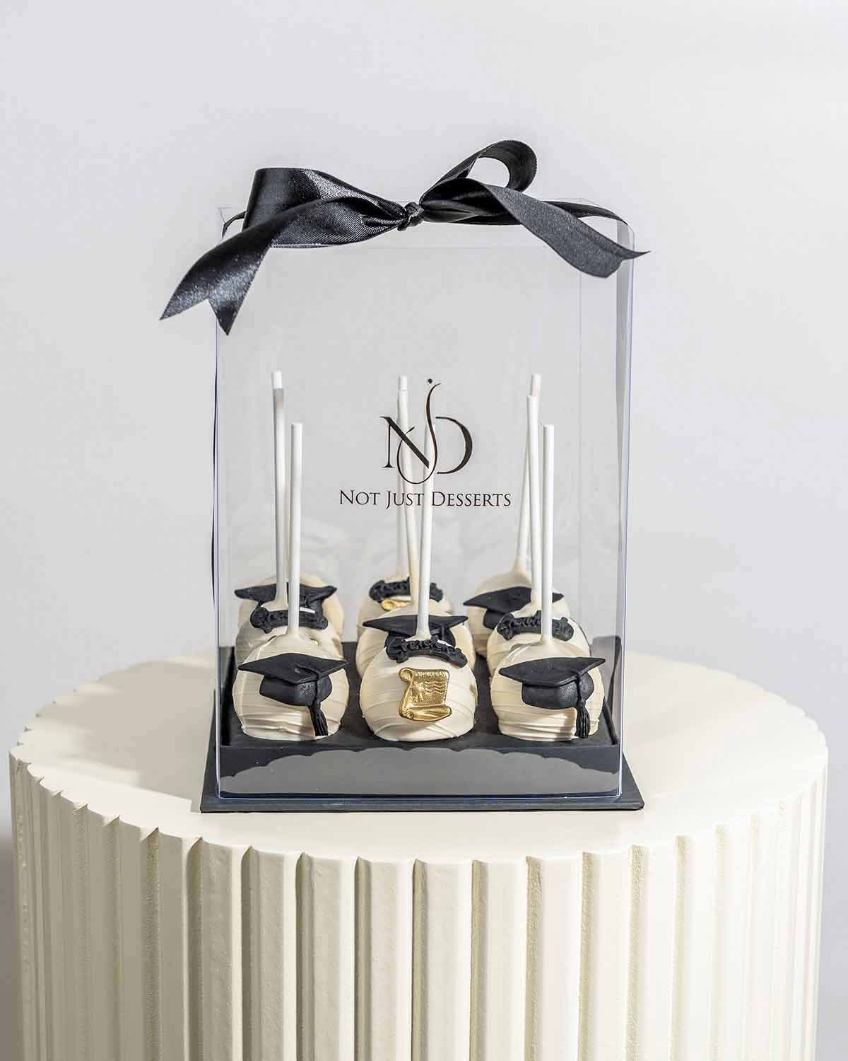 White Chocolate Graduation Cake Pops by NJDChocolate & ConfectioneryYour Gift Contains:• 9 x cake pops• Flavors available: Chocolate/Vanilla/Red Velvet• Chocolate Weight: 530gms approx.• Box Size: 16x16x20cmHandling and Storage • Keep away from direct hea