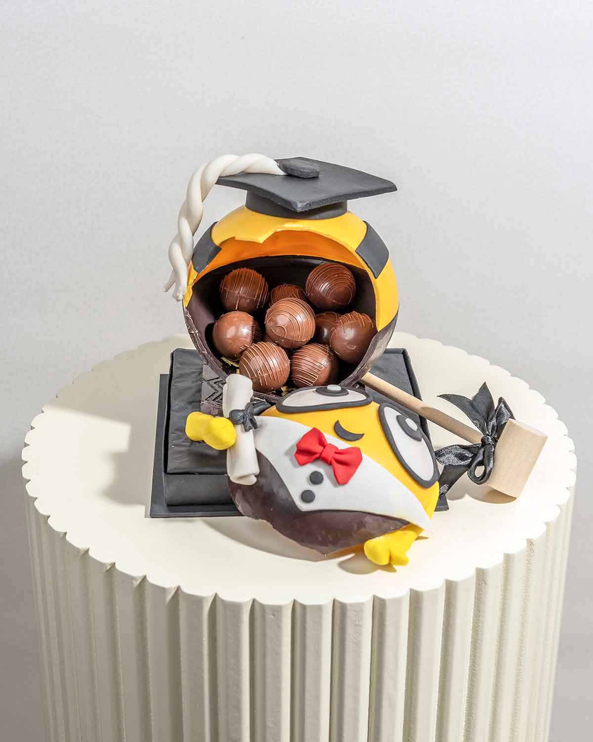 Graduation Theme Minion by NJDChocolate & ConfectioneryYour Gift Contains:• 1 x Graduation Minion theme smashable ball • 10 assorted Milk Chocolate Truffles • Total weight of the chocolate: 575g• Flavors: Pistachio, Hazelnut, Speculoos, Peanut Butter and