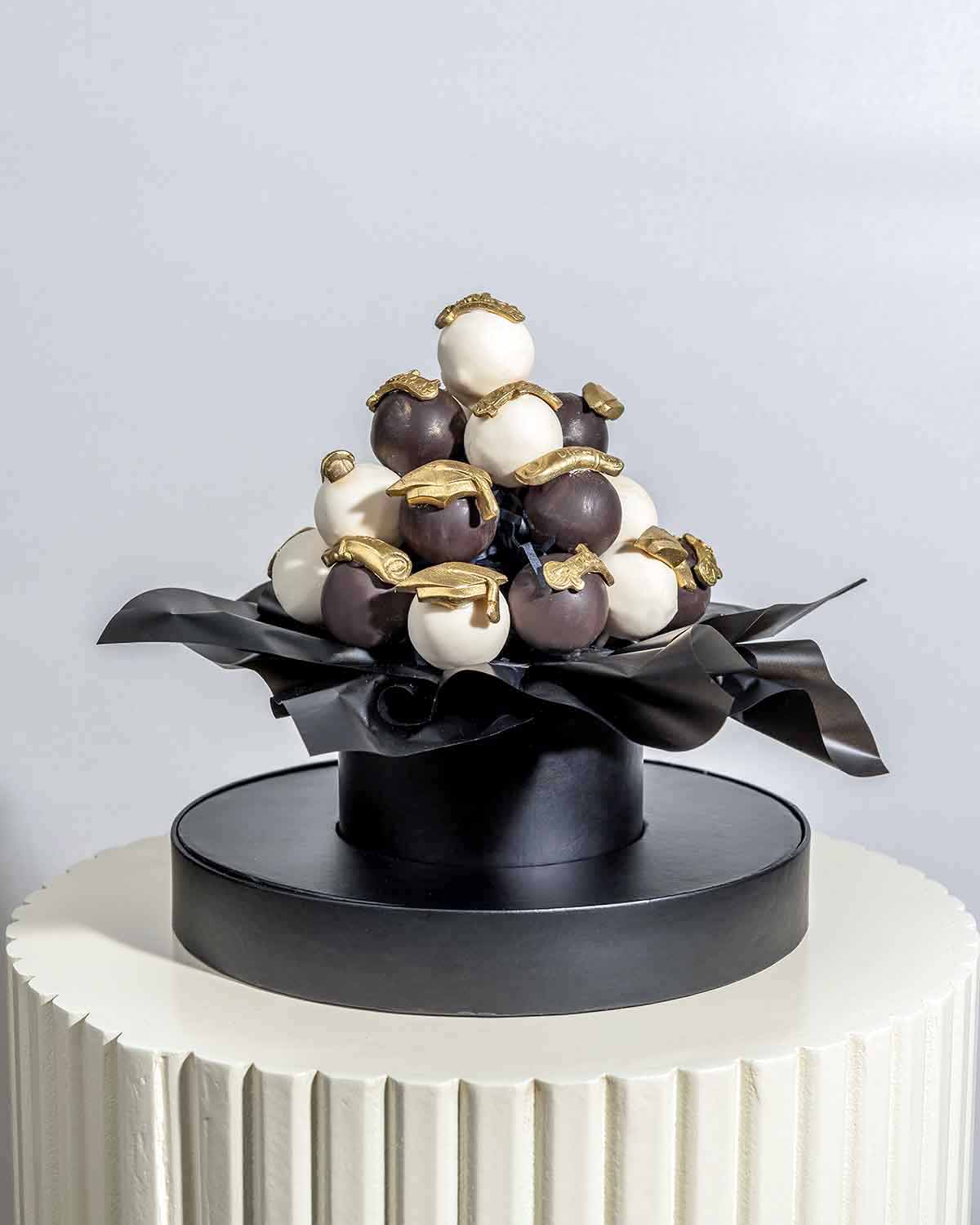 Graduation theme Cake pops AssortmentChocolate & ConfectioneryYour Gift Contains:• 24 x assorted cake pops in Graduation theme• Cake Flavors: Chocolate/Vanilla/Red Velvet• Chocolate Weight: 580g• Box Size: 21x21x25.5cmHandling and Storage • Keep away from