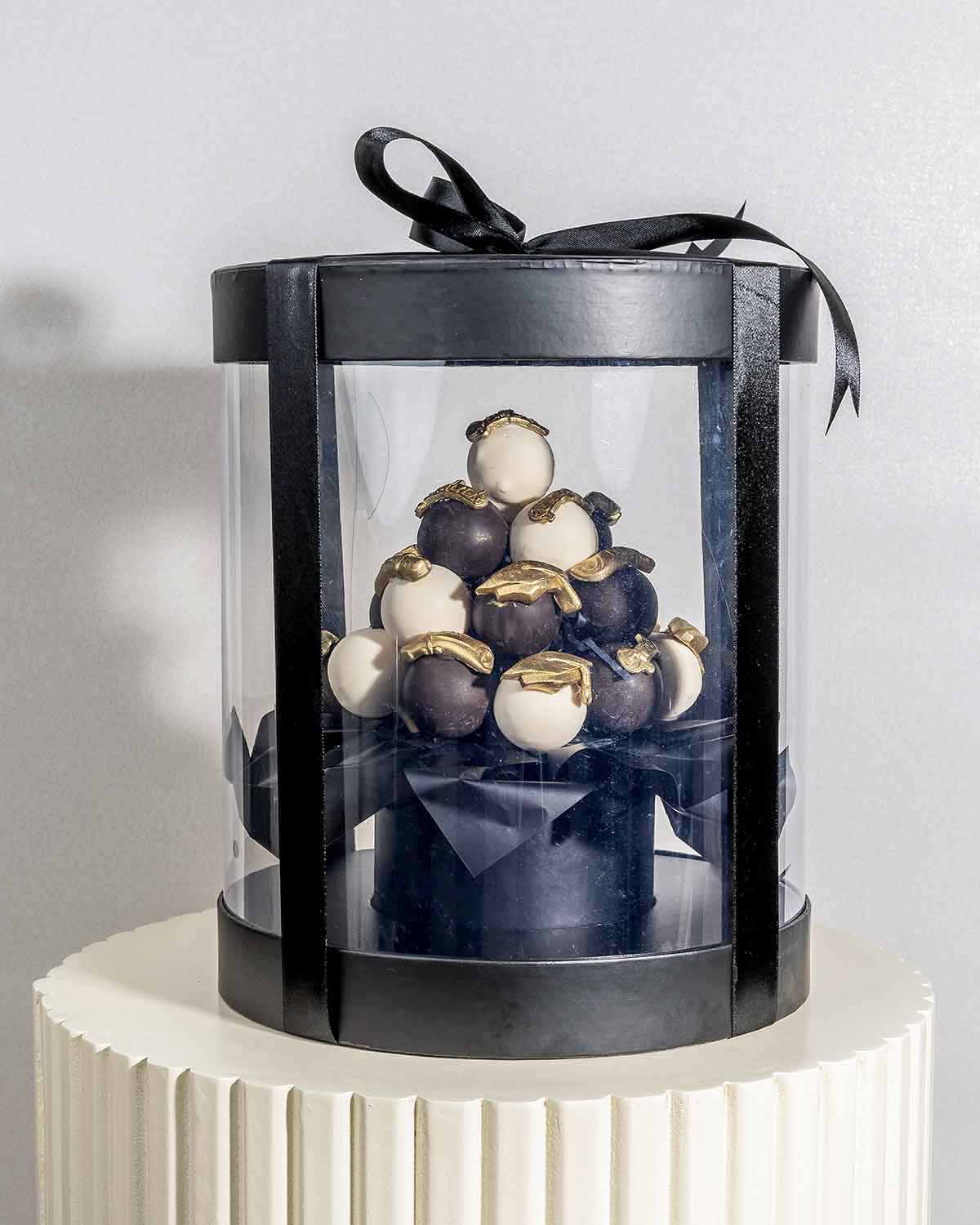 Graduation theme Cake pops AssortmentChocolate & ConfectioneryYour Gift Contains:• 24 x assorted cake pops in Graduation theme• Cake Flavors: Chocolate/Vanilla/Red Velvet• Chocolate Weight: 580g• Box Size: 21x21x25.5cmHandling and Storage • Keep away from