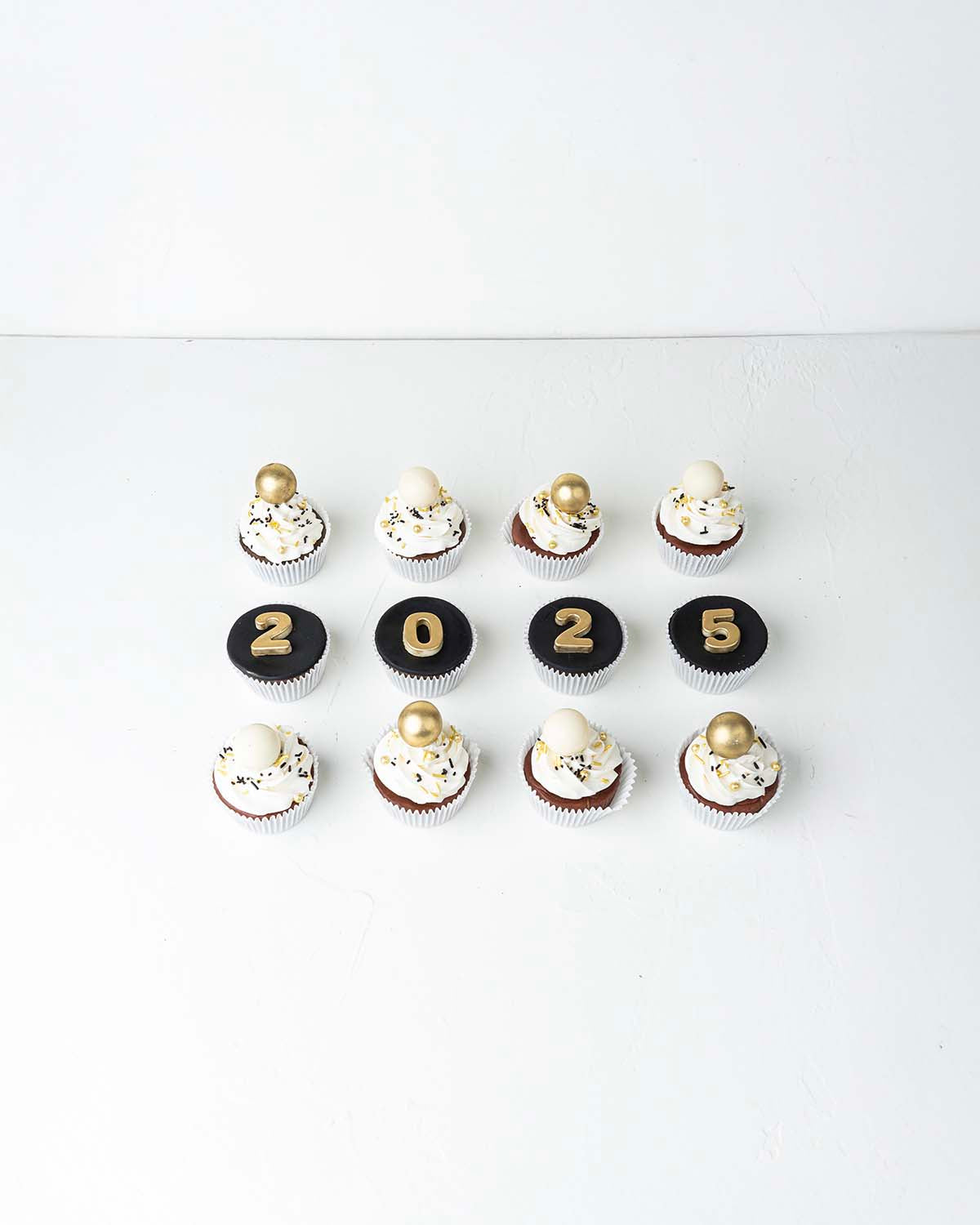 12 New Year Theme CupcakesChocolate & ConfectioneryYour Gift Contains:• 12 Year 2025 Theme cupcakes• 8 assorted White and gold truffles• Flavors: Pistachio, Hazelnut, Speculoos, Peanut Butter and Roche• Flavor: Chocolate/Vanilla/Red Velvet• Box Size: 34 x