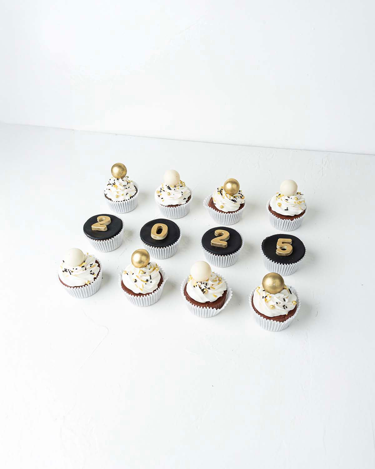 12 New Year Theme CupcakesChocolate & ConfectioneryYour Gift Contains:• 12 Year 2025 Theme cupcakes• 8 assorted White and gold truffles• Flavors: Pistachio, Hazelnut, Speculoos, Peanut Butter and Roche• Flavor: Chocolate/Vanilla/Red Velvet• Box Size: 34 x
