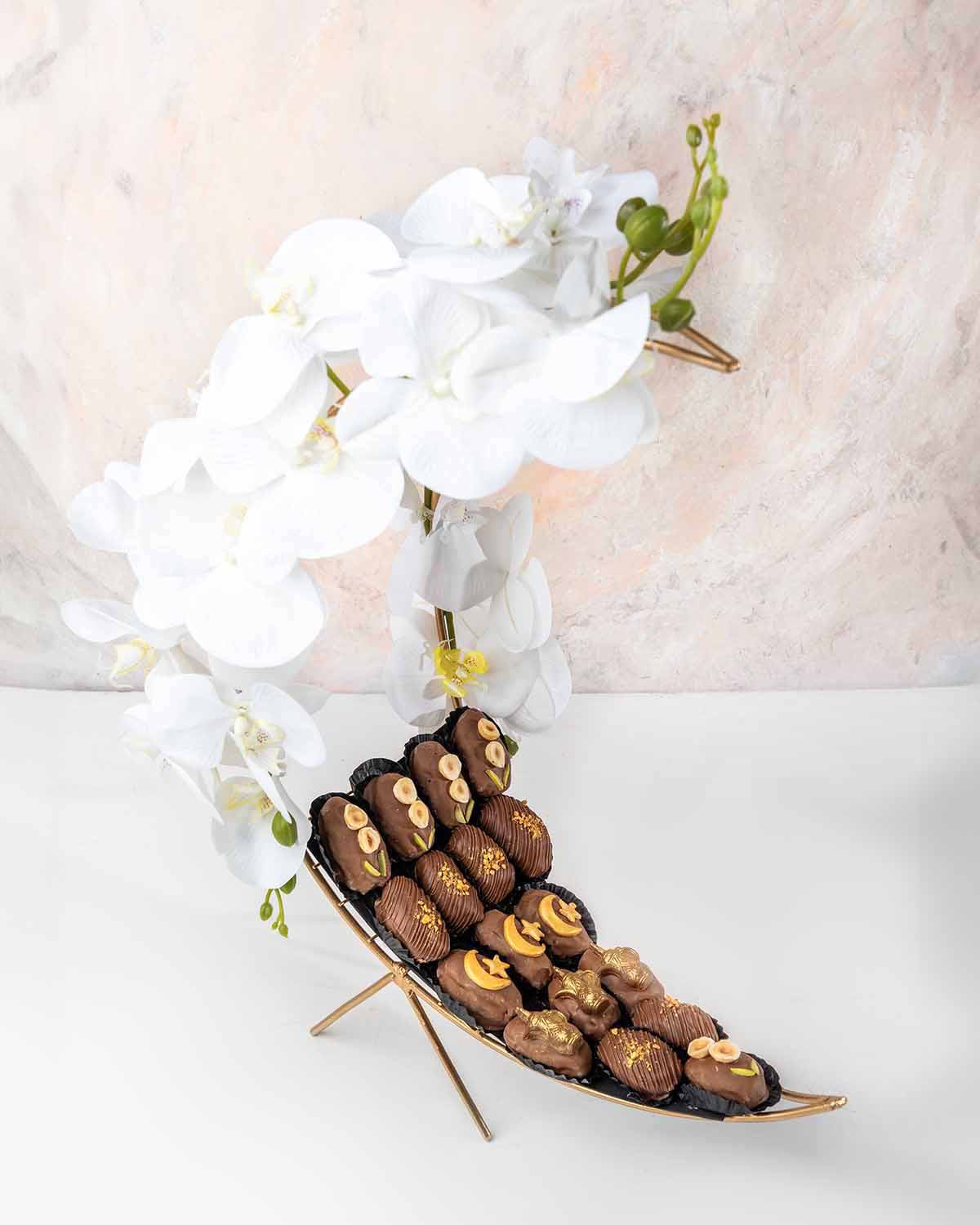 Crescent Dates Collection by NJDChocolate & ConfectioneryYour Gift Contains:• 17 x Hand designed Milk Chocolate covered dates with assorted nuts• Artificial flower arrangement• Tray Size: 30x16x36cmHandling and Storage • Keep away from direct heat and sun