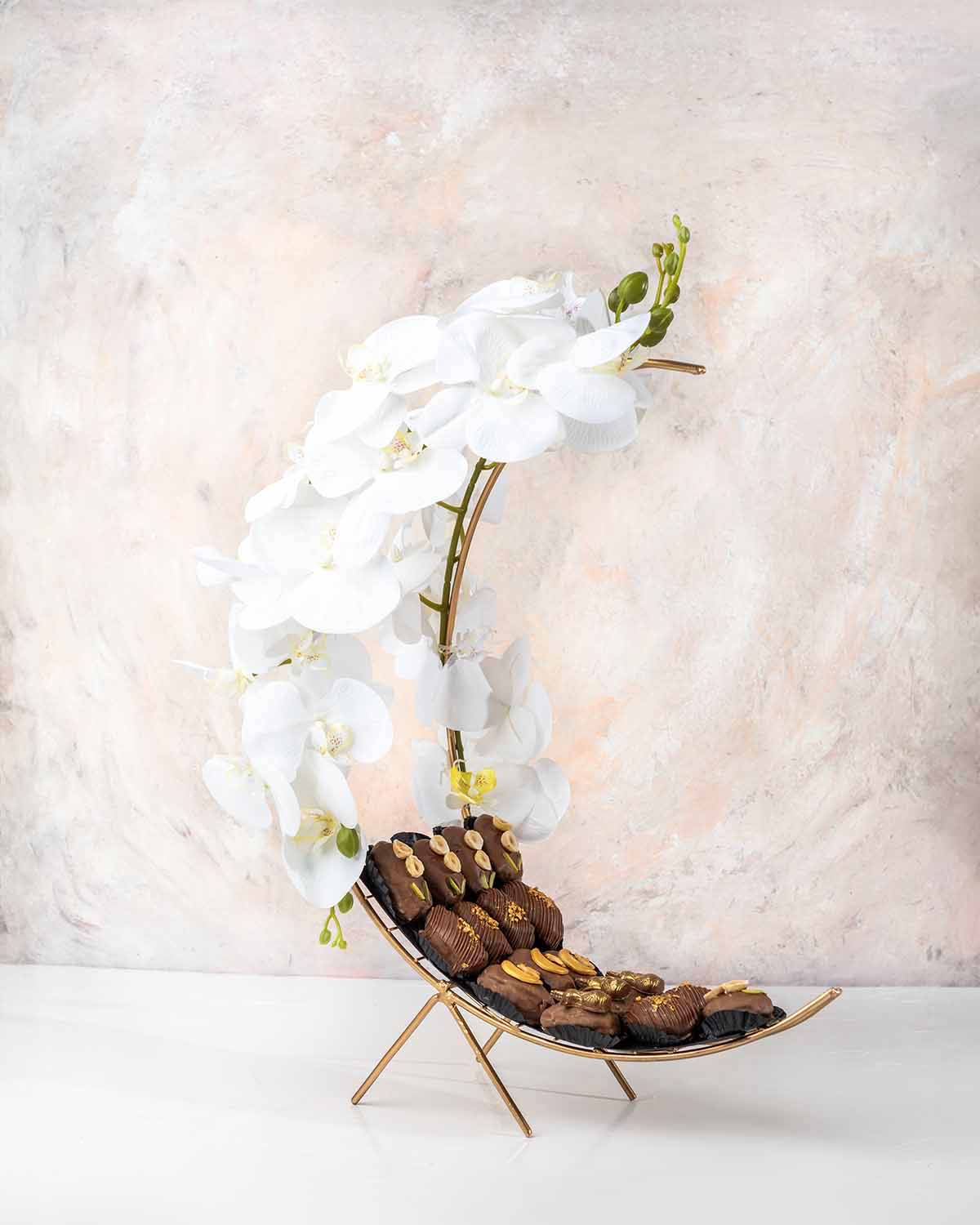 Crescent Dates Collection by NJDChocolate & ConfectioneryYour Gift Contains:• 17 x Hand designed Milk Chocolate covered dates with assorted nuts• Artificial flower arrangement• Tray Size: 30x16x36cmHandling and Storage • Keep away from direct heat and sun