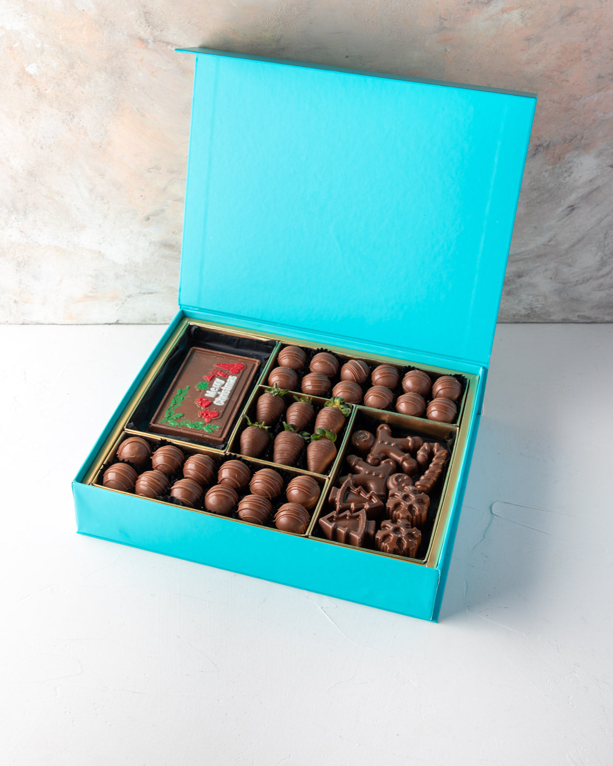 Assorted Christmas Greetings BoxChocolate & ConfectioneryYour Gift Contains: • 24 pieces Milk Chocolate Truffles in Peanut butter, Rice Crispy, Pistachio, Sepculoos and Hazelnut Gandoua and Pistachio Praline flavors • 50gms Milk Chocolate bar with Merry C