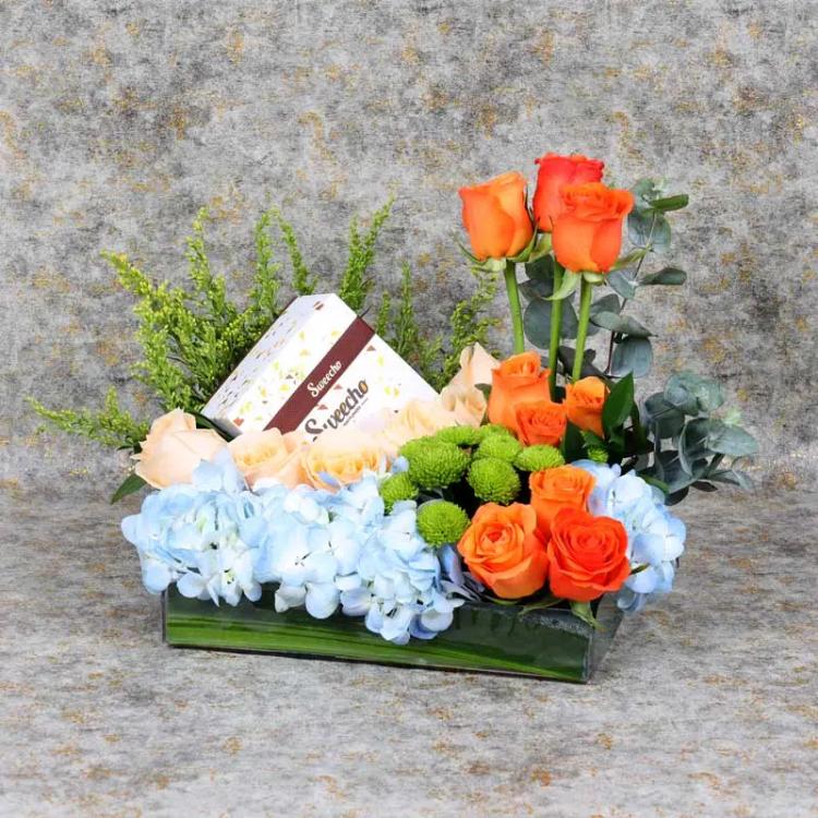 Sky Flowers and Chocolate ArrangementChocolate & ConfectioneryPremium Assorted Chocolates 250 gm By Sweecho, 1 Blue Hydrangea, 9 Orange Roses, 6 Peach Roses, 2 Stems Green Button Chrysanthemums, 3 Stems Solidago, Leaves : 3 Stems Eucalyptus, Prepare in Ac