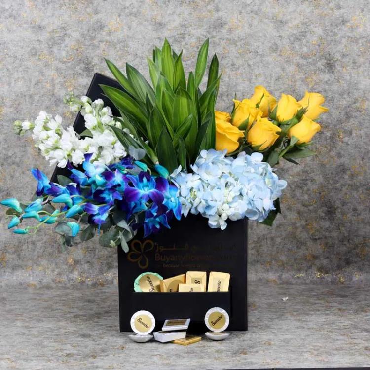 Alpha Flowers and Chocolate BoxChocolate & ConfectioneryPremium Assorted Chocolates 100 gm By Sweecho, 1 Blue Hydrangea, 5 White Matthiola, 5 Blue Orchid, 8 Yellow Roses, Leaves : 2 Song of Jamaica, Prepared in Square Black Box.