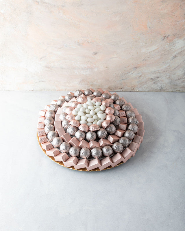 Rose Gold Arrangement by NJDChocolate & ConfectioneryYOUR GIFT CONTAINS Content: Assorted Milk Belgian chocolates 104pcs White Drageè 150gms Flavors: Assorted Chocolates and truffles filled with praline, ganache, Biscoff, roasted nuts and wafer fillings T