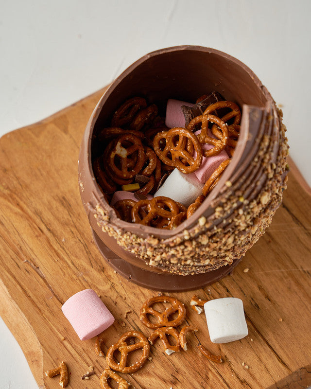 Hazelnut Crunch Easter EggChocolate & ConfectioneryYour Gift Contains: • 600 grams milk chocolate roasted Hazelnut egg • Fillings: Marshmallows, Pretzels, Drageè • Box Size: 13x13x26cm Handling and Storage • Keep away from direct heat and sunlight • Best