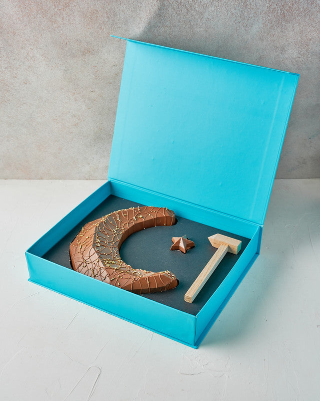 Edible Crescent by NJDChocolate & ConfectioneryYour Gift Contains: • 300gms Milk chocolate Crescent and star • 15 milk chocolate truffles in assorted flavours: Pistachio, Peanut Butter, Lotus and Roche • Hammer • Box Size: LxBxH: 31x25.5x6cm Handling and