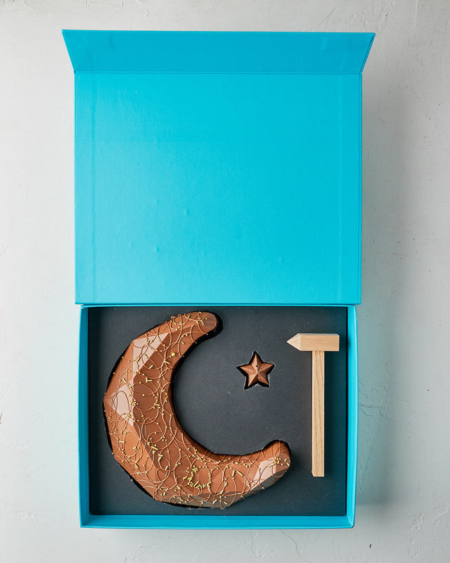 Edible Crescent by NJDChocolate & ConfectioneryYour Gift Contains: • 300gms Milk chocolate Crescent and star • 15 milk chocolate truffles in assorted flavours: Pistachio, Peanut Butter, Lotus and Roche • Hammer • Box Size: LxBxH: 31x25.5x6cm Handling and