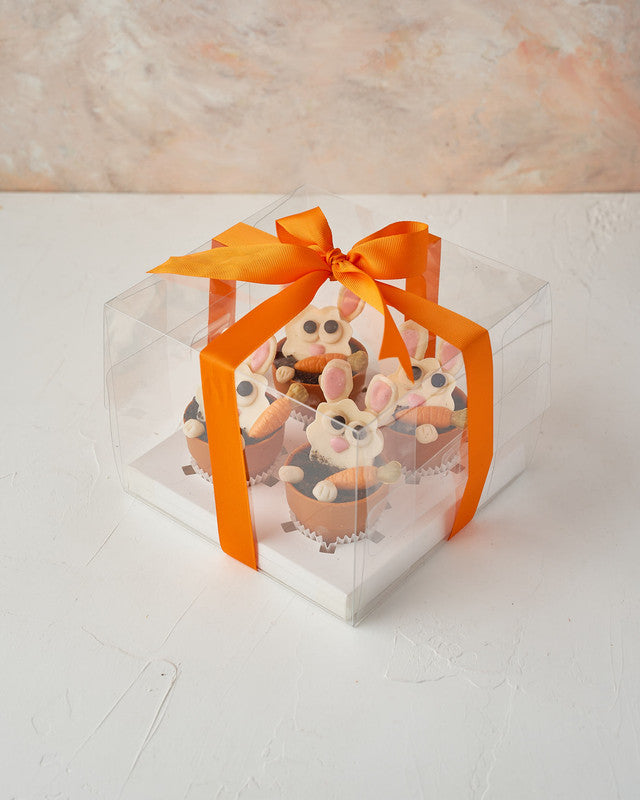 Bunny in PotsChocolate & ConfectioneryYour Gift Contains: • 4 White chocolate bunny face • Edible Pots with vanilla and hazelnut ganache • Box Size: 18x18x18cm Handling and Storage • Keep away from direct heat and sunlight • Best stored between 8-15 °C •