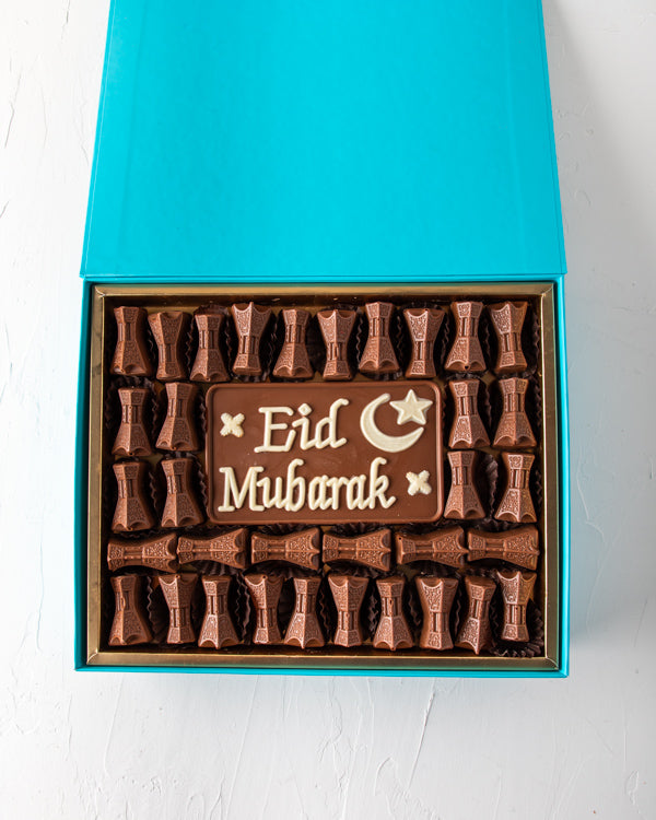 EID Greetings 34pcsSweetsYOUR GIFT CONTAINS 34pcs assorted milk chocolates filled with hazelnut, dates and Peanut butter, lotus and pistachio praline flavor 50gms Milk chocolate slab with EID Mubarak Message Box/Tray Size: LxBxH: 31x 25.5x6cm HANDLING AND