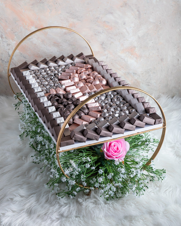 Chocolate Arrangement by NJDChocolate & ConfectioneryApprox. 3kg chocolates on the beautiful tray decorated with faux flowers making a good center piece. 8 fillings: Nutella, Peanut Butter, Salted Caramel, Roasted Nuts, Biscoff, Lotus, Ganache and Praline